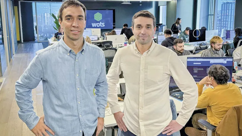 Dos integrantes del equipo de Wots en sus oficinas, con el resto del equipo trabajando al fondo.
